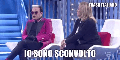 a man in a pink suit is sitting next to a woman in a black suit and sunglasses .