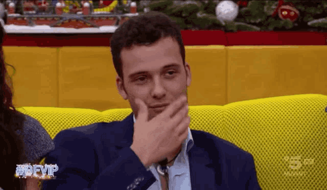 a man in a suit is sitting on a yellow couch in front of a christmas tree and a sign that says #bevip