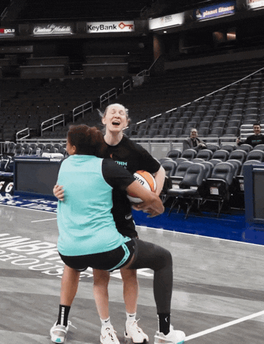 two women hugging on a basketball court in front of a keybank ad