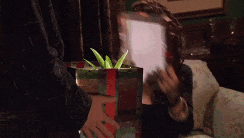 a woman is holding a gift box with a red ribbon