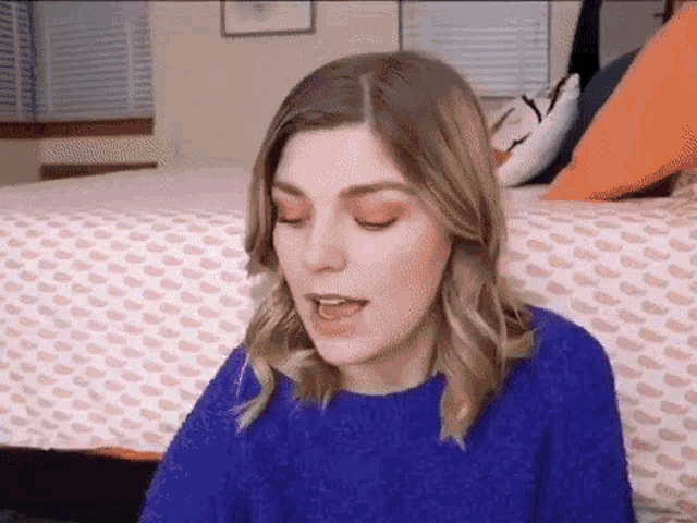 a woman in a blue sweater is sitting on a bed and talking .