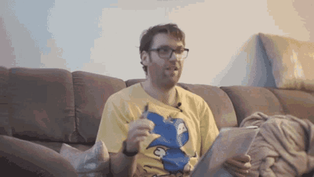 a man is sitting on a couch eating a snack and reading a book
