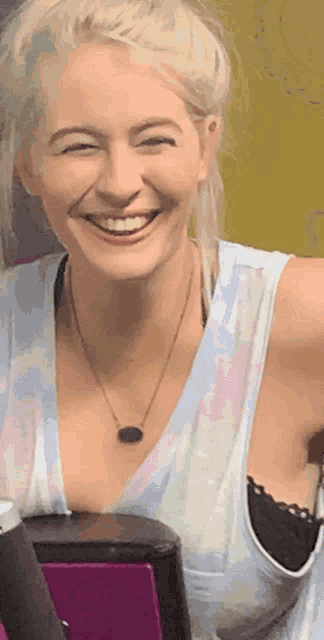 a woman wearing a tank top and necklace is smiling