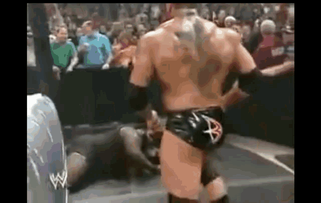 a wrestler is standing in front of a crowd while a wrestler is laying on the ground .