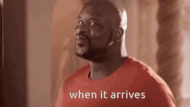 a man in a red shirt is standing in front of a mirror and says when it arrives .