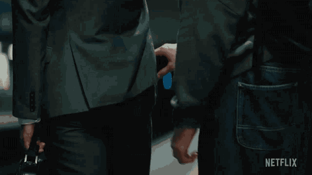 a man in a suit is standing next to another man in a black shirt with netflix written on the bottom