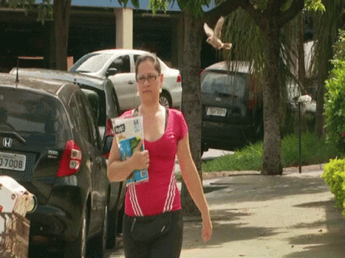 a woman in a pink shirt is walking down the street with a magazine in her hand and a honda car behind her