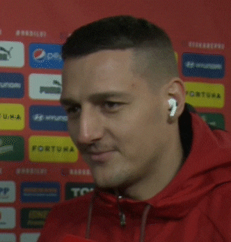 a man wearing ear buds talks into a microphone in front of a wall with logos for pepsi and puma