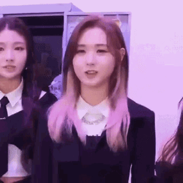 a group of girls are standing next to each other in a locker room . one of the girls has pink hair .
