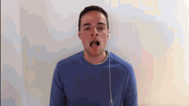 a man wearing a blue sweater and ear buds is singing into a microphone