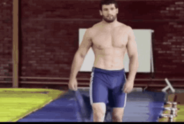 a shirtless man in blue shorts is walking on a mat .