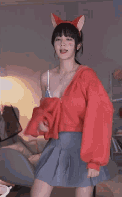 a girl wearing a red sweater and a blue pleated skirt is standing in a room .