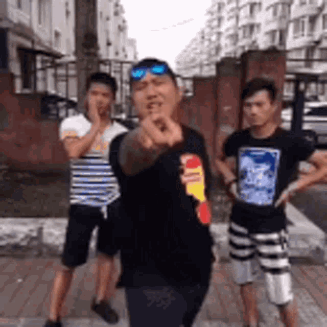 three men are standing on a sidewalk and one of them is pointing at the camera
