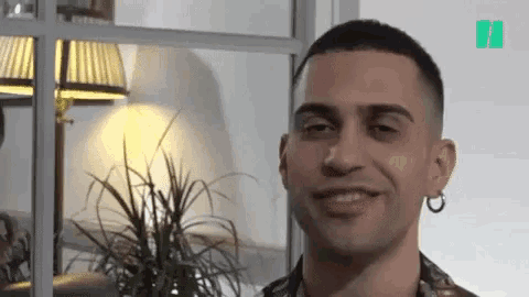a young man with earrings on his ears is smiling in front of a lamp .