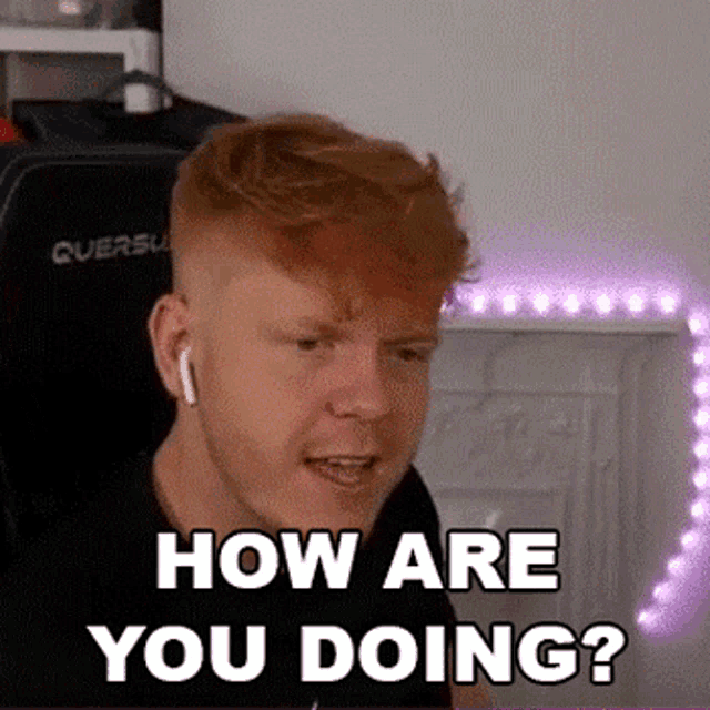 a man with red hair is sitting in a chair with headphones on and asking how are you doing .
