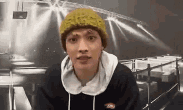 a young man wearing a yellow hat and a black hoodie is making a funny face .