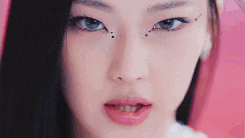 a close up of a woman 's face with a pink background and black dots on her eyes .