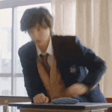 a man in a suit and tie is sitting at a desk in a classroom with his hands on his hips .