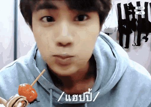 a man in a blue hoodie is eating a candy on a stick .