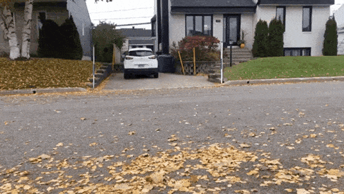 a white car is parked in front of a house with leaves on the ground