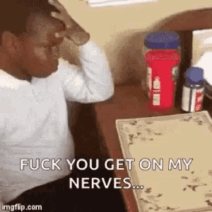 a man is sitting at a desk with his hand on his head and says `` fuck you get on my nerves `` .