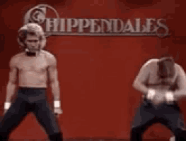 two shirtless men are dancing in front of a chippendale 's sign