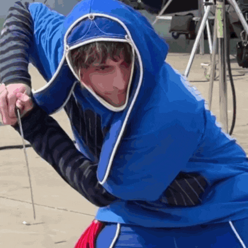 a man wearing a blue hooded jacket is holding a stick