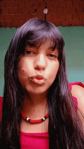 a woman wearing a red top and a red necklace blows a kiss