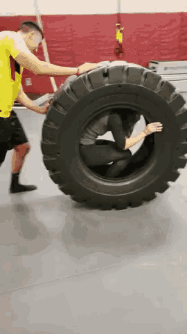 a man is pushing a woman through a tire in a gym