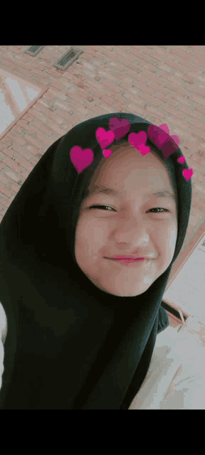 a young girl wearing a black hijab with pink hearts on it is smiling .