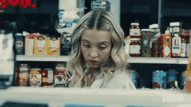 a woman is standing in front of a counter in a grocery store looking at something .