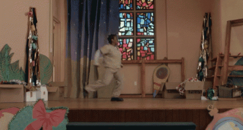 a man is running on a stage in front of a stained glass window with the letter t on it