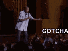 a man is standing on a stage with a microphone and the words gotcha bitch above him