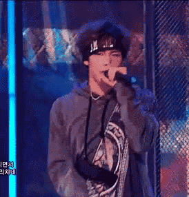 a young man wearing a headband is singing into a microphone on a stage .