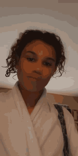 a young woman with curly hair is wearing a white robe and a leopard print purse .