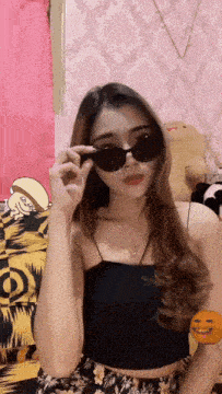 a woman wearing sunglasses and a black tank top looks at the camera