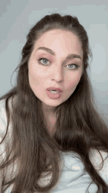 a woman with long brown hair and blue eyes is making a face