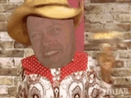 a man wearing a cowboy hat and a red scarf is smiling .