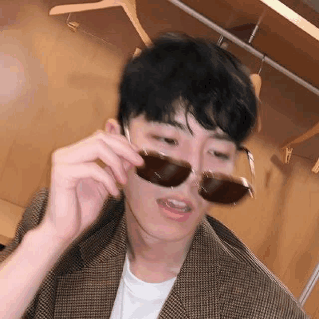 a young man wearing sunglasses and a plaid jacket .