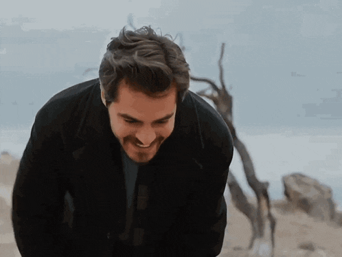 a man in a black jacket is smiling in front of a tree branch