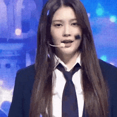 a young woman wearing a suit and tie is standing in front of a microphone .