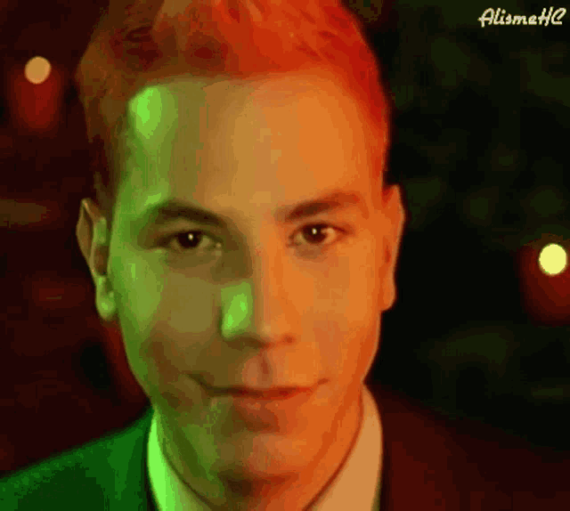 a man with red hair is smiling in front of a christmas tree in a green suit