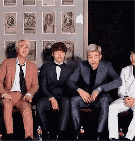 a group of men in suits are sitting next to each other in front of a wall with pictures on it .