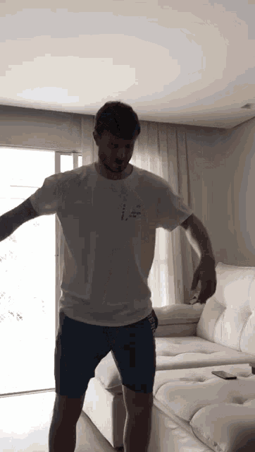 a man in a white t-shirt and blue shorts is standing in front of a white couch