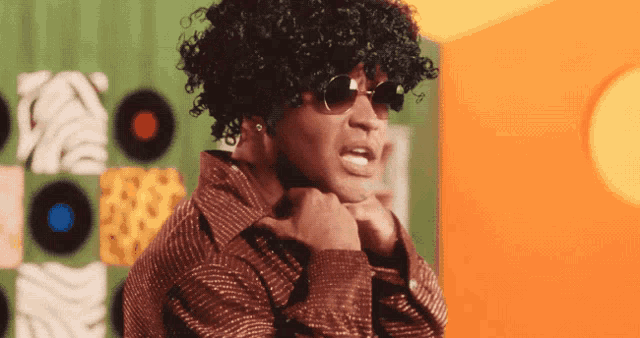 a man wearing a wig and sunglasses stands in front of a wall with records on it