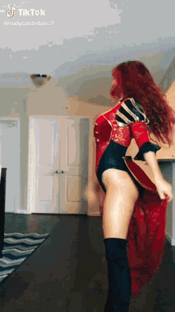a woman with red hair is standing in a living room wearing a red and black outfit .