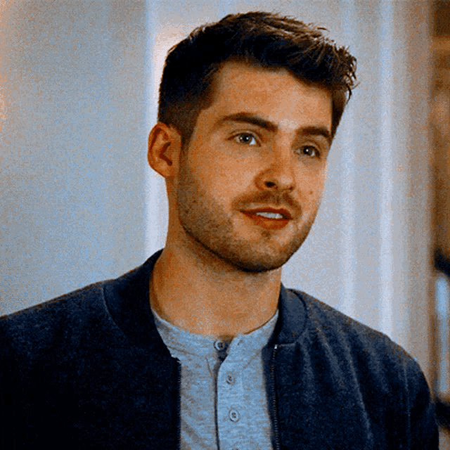 a young man with a beard is wearing a blue jacket and a grey shirt