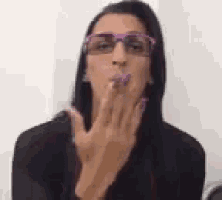 a woman wearing glasses is blowing a kiss to the camera .