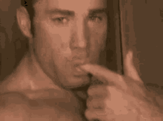 a man without a shirt is licking his lips .