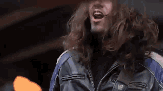 a man with long hair is singing into a microphone while playing a guitar .